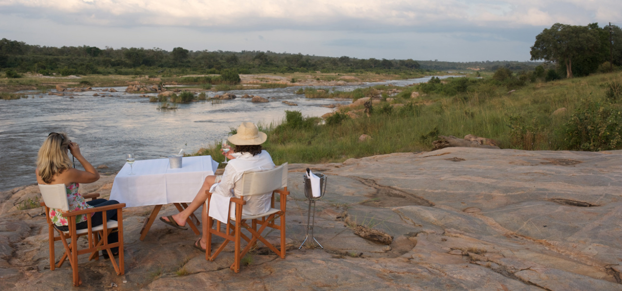 Two people sitting at a table with drinks enjoying a scenic view of Kruger Park at Mjejane River Lodge.