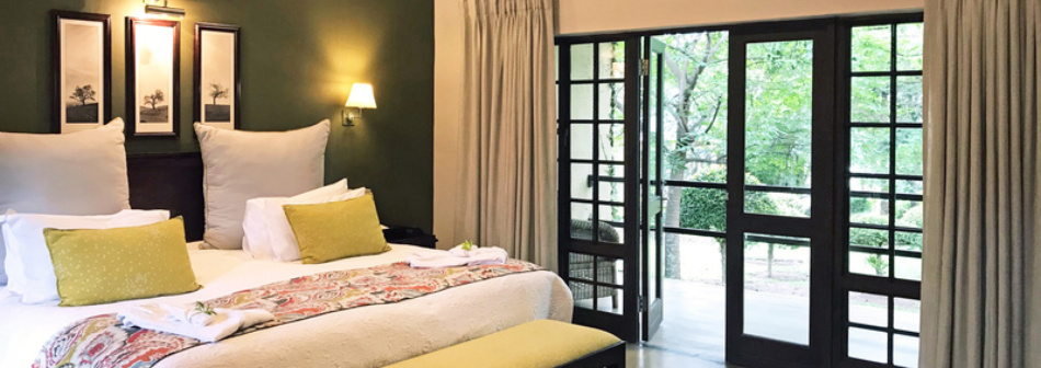 An elegant Perry's Bridge Hollow Boutique hotel room featuring a cozy bed and glass doors opening to a lush garden view.